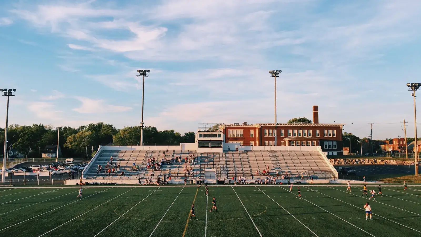 American football field with yard lines, goalposts and a small stand beside tall floodlight poles