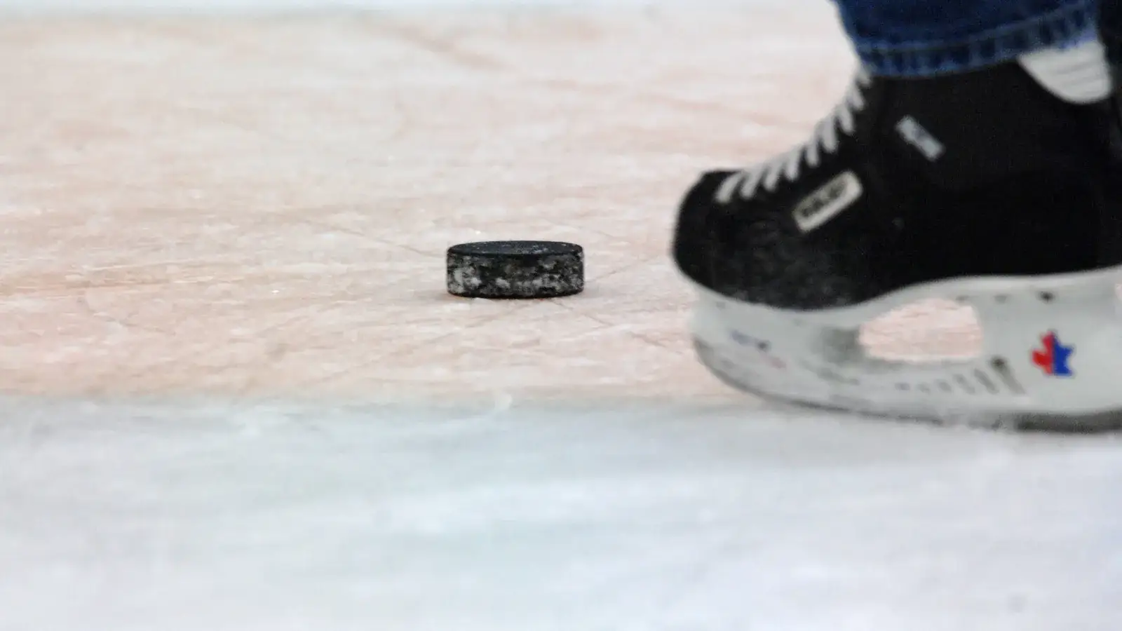 Ice hockey puck on scratched ice beside a skate blade