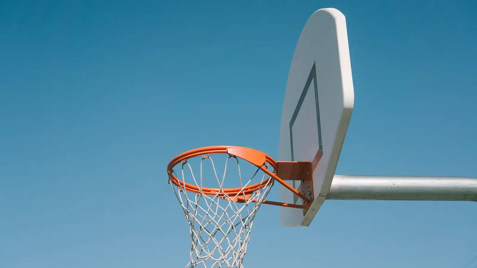 Basketball backboard and orange rim against a clear blue sky