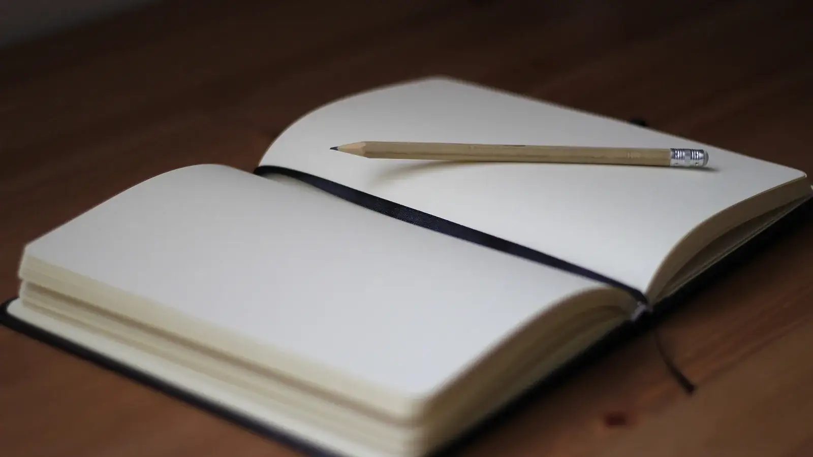 Open blank notebook with a pencil lying across the pages on a wooden table