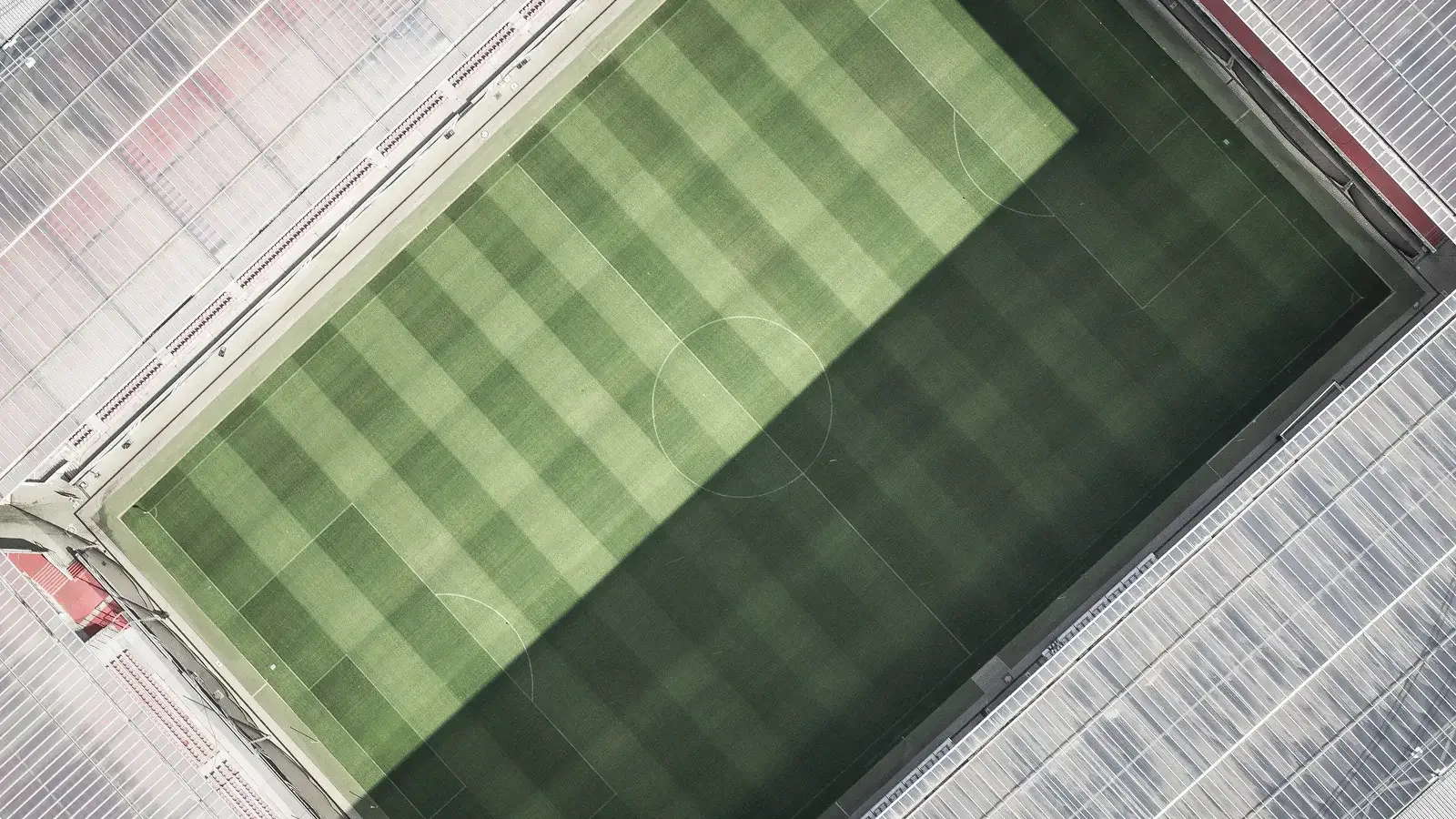 Drone view straight down onto a striped football pitch inside an empty stadium bowl