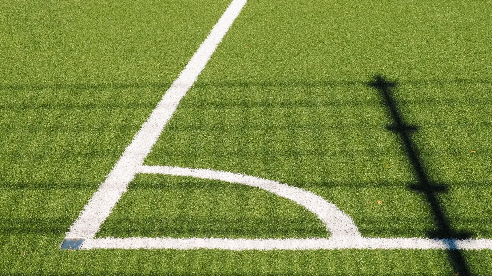 Close view of a freshly painted corner arc on a striped green football pitch