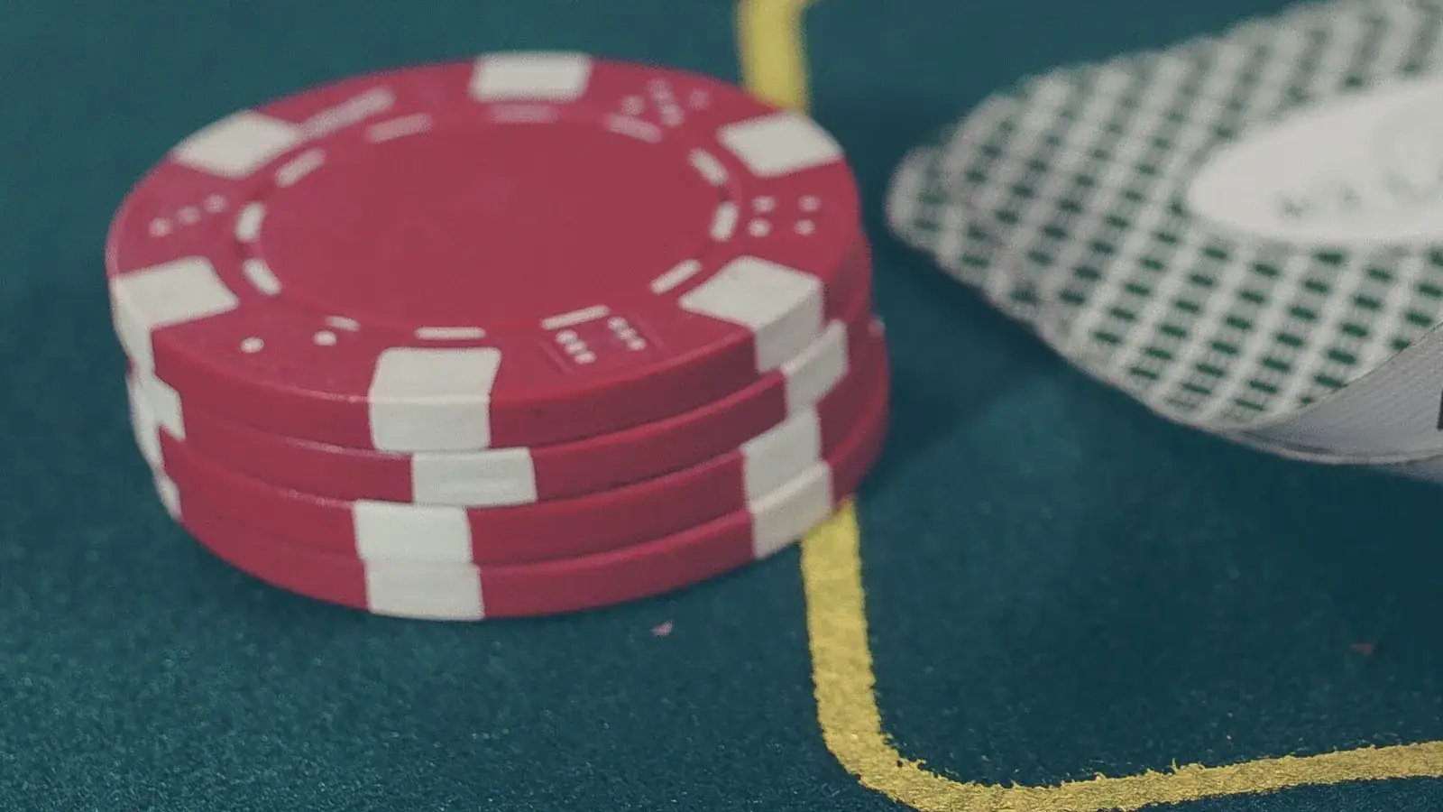 Stacks of red, white and green poker chips on a green felt table, cards behind