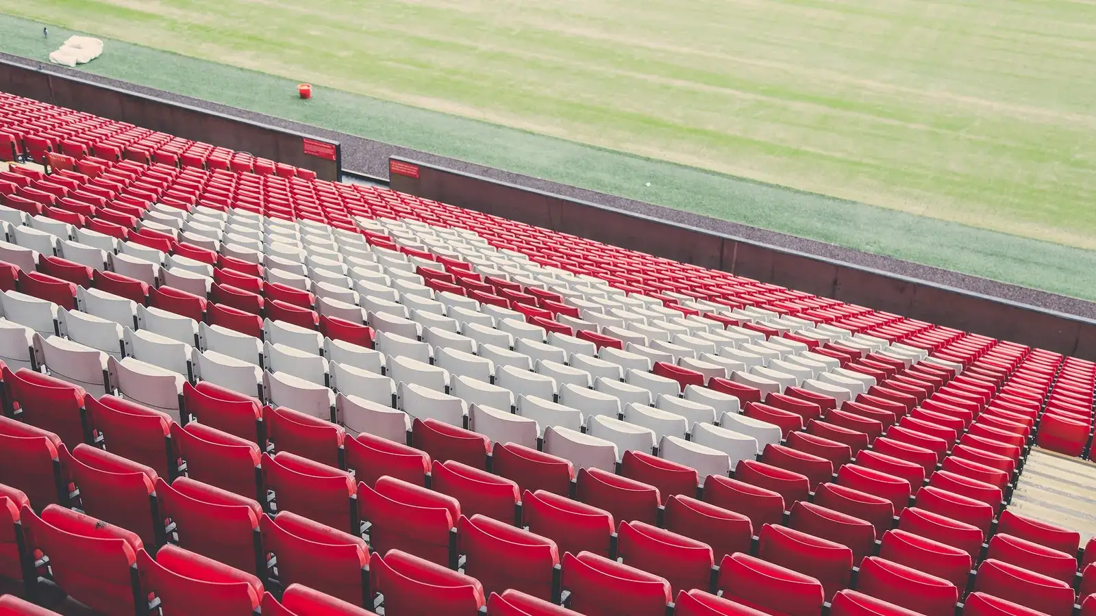 Rows of red and white stadium seats beside the edge of a football pitch