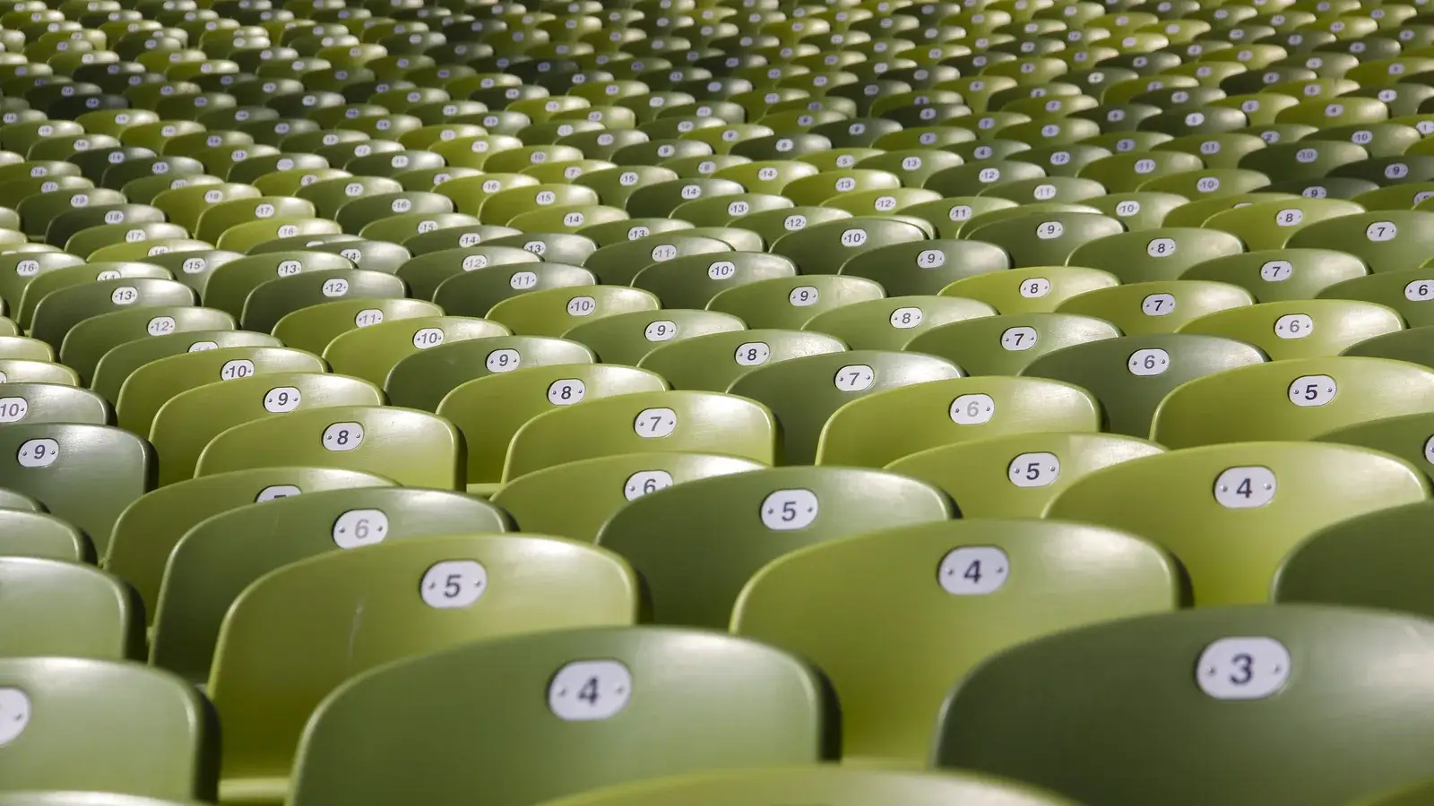 Rows of empty green stadium seats under a tented roof