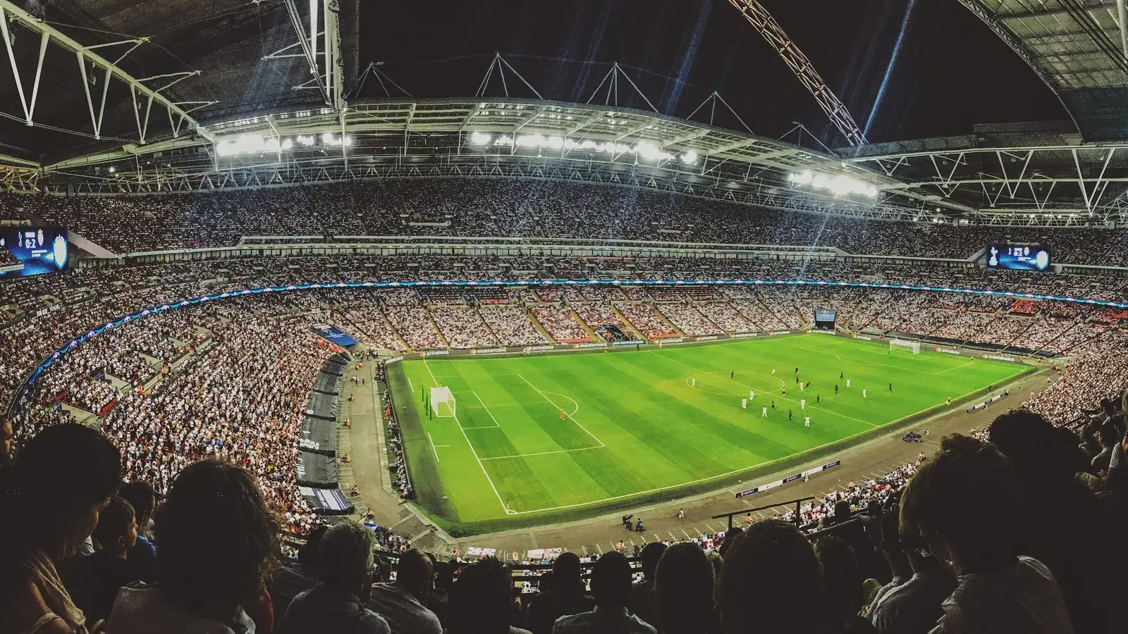 Panoramic view of a packed football stadium under its lit roof arch during an evening match