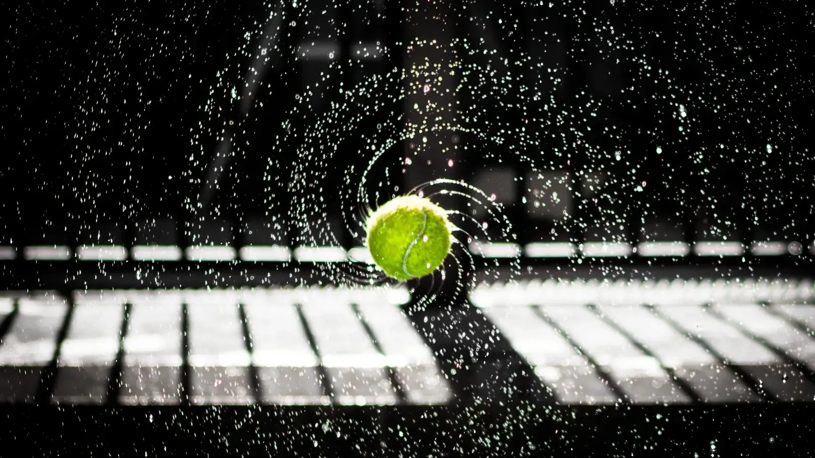Tennis ball hitting a wet court at night, water spraying in a ring of droplets