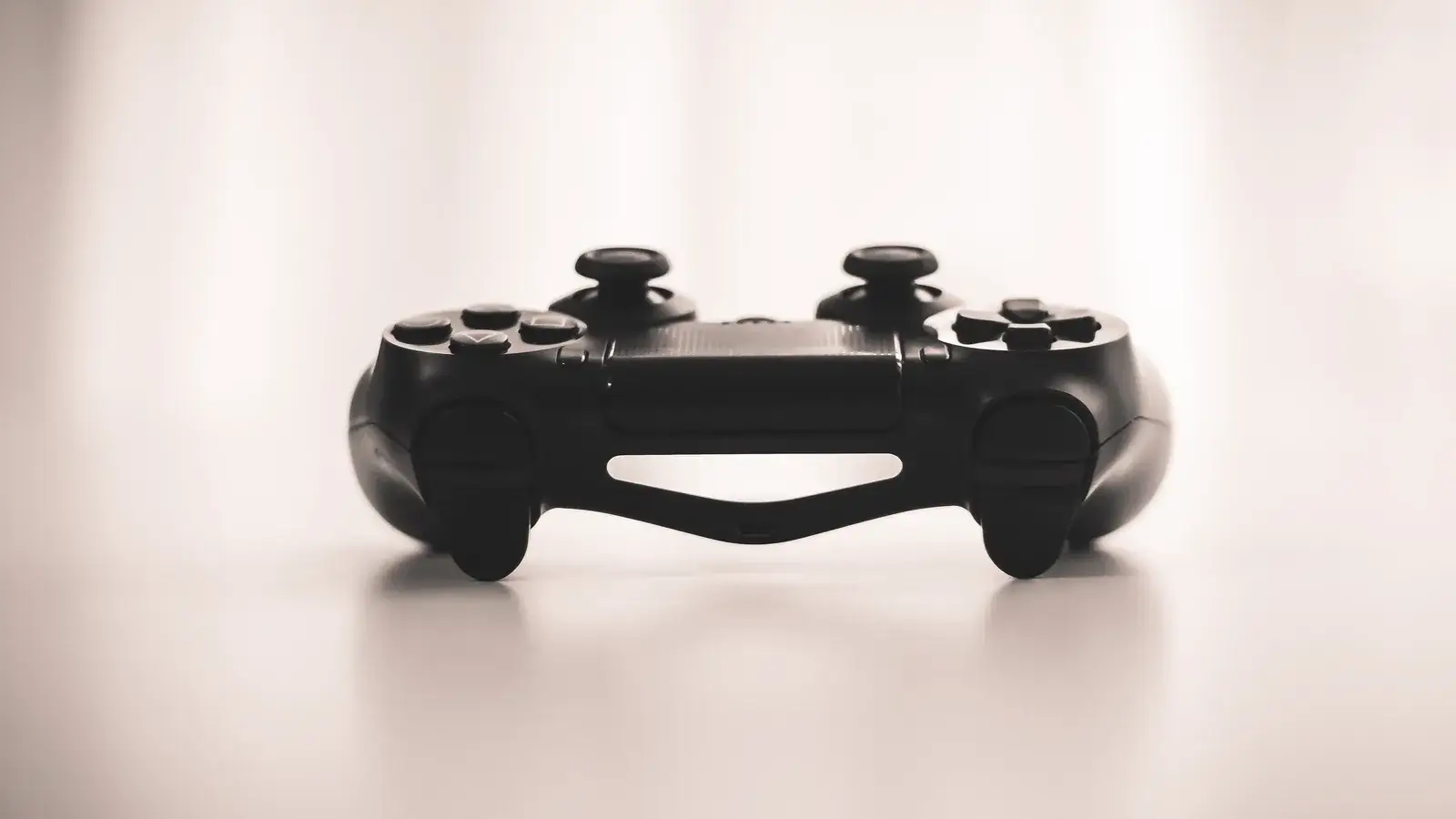 Black game controller standing on a pale reflective surface in soft light