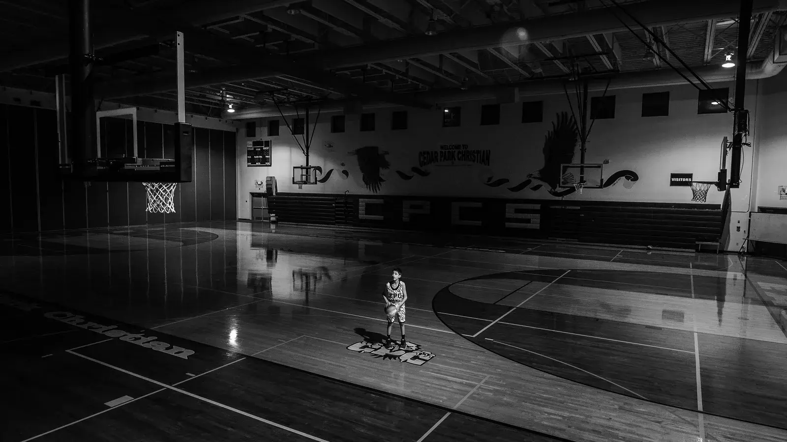 Black and white indoor basketball gym, a lone player standing at centre court