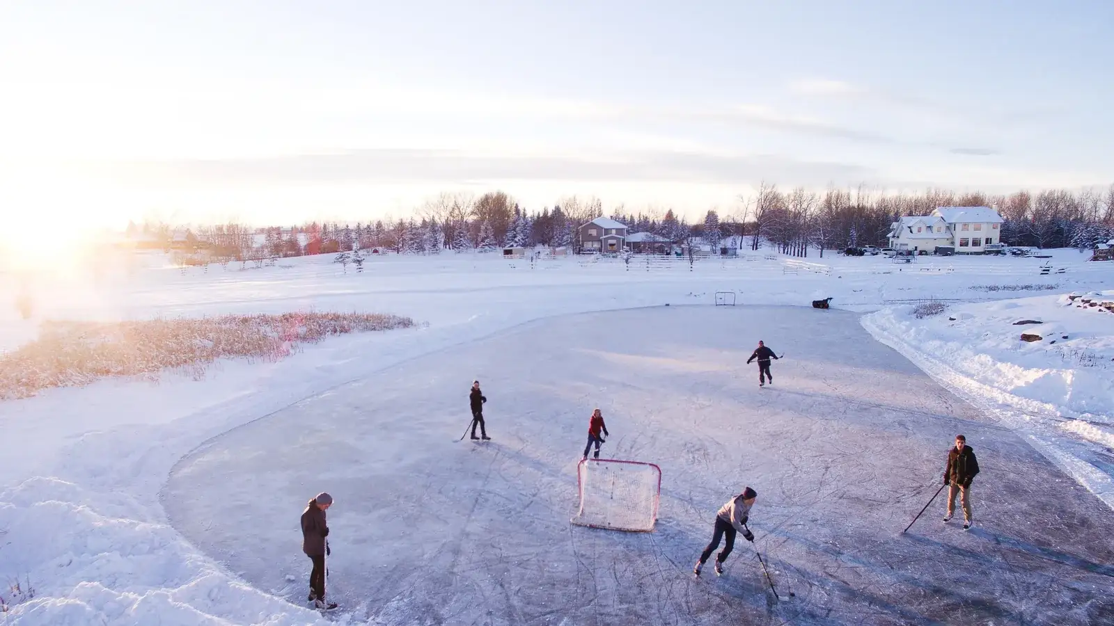 Pond hockey on a frozen lake at sunrise, players and a small goal on the ice