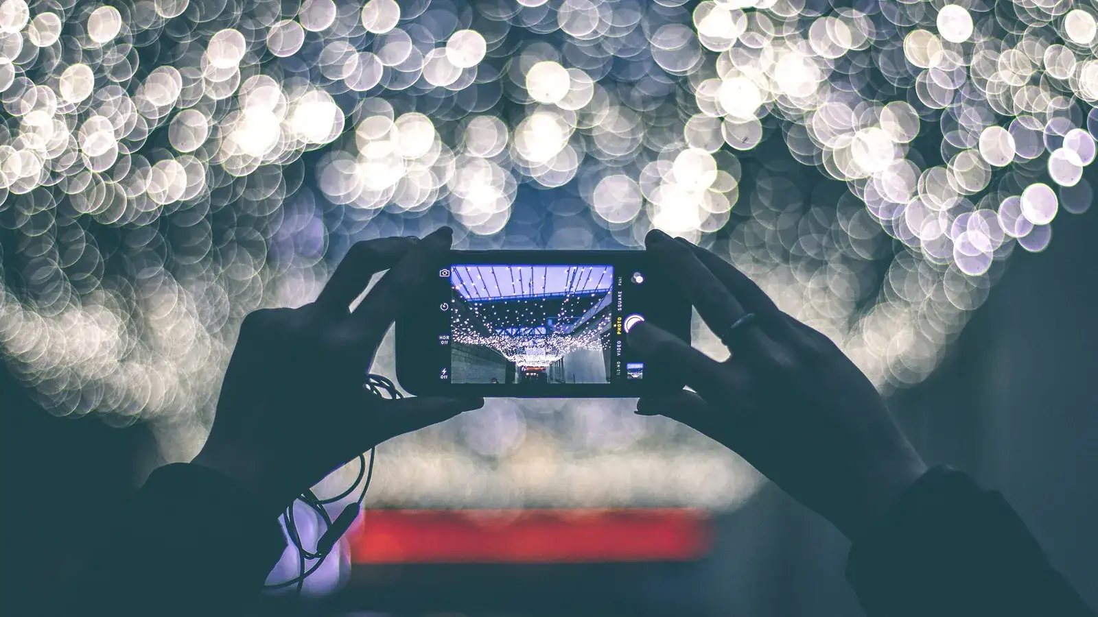 Hands holding a phone up to film a stage, lights blurred into bokeh