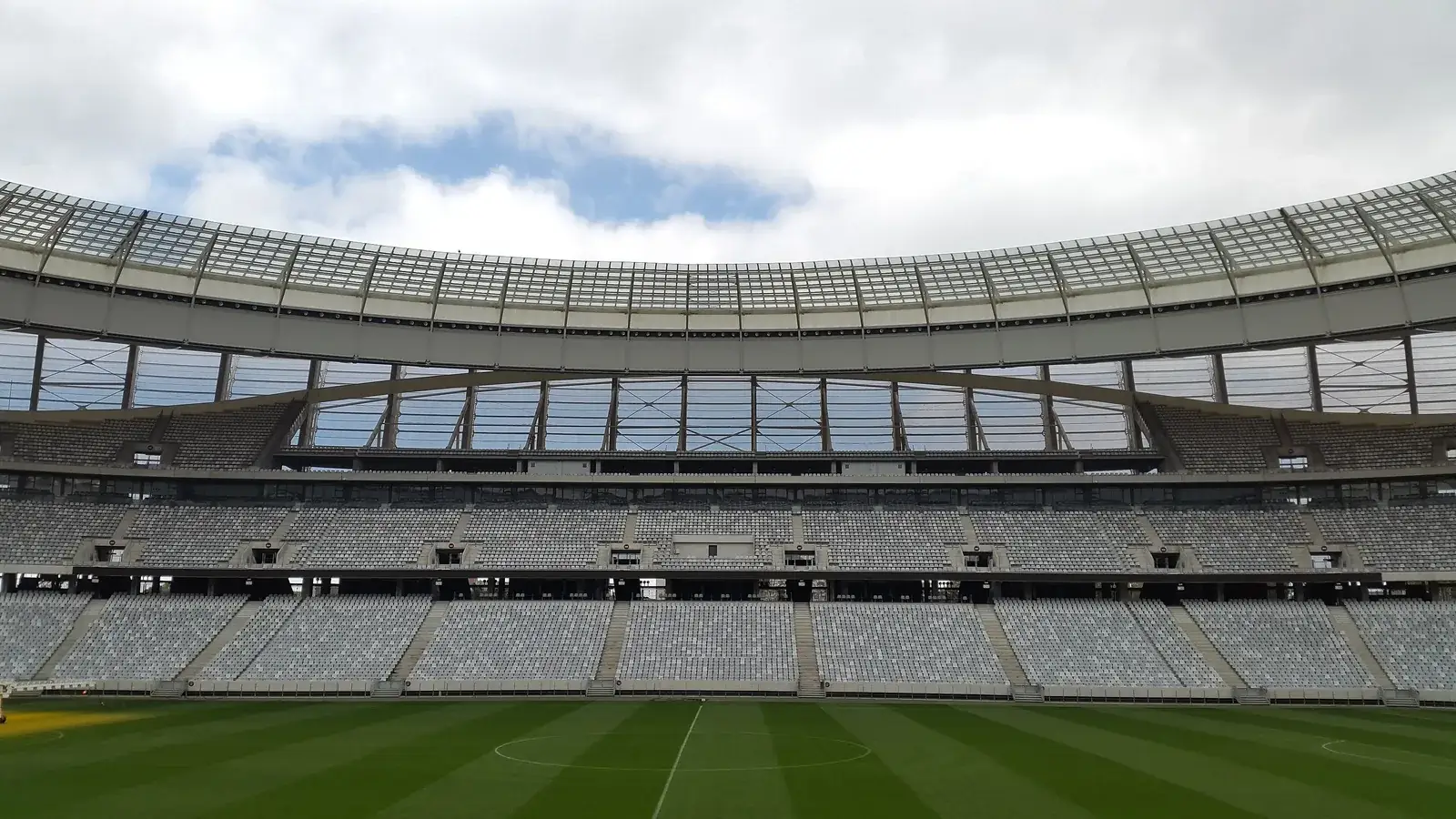 Inside an empty modern football stadium, white curved roof above green pitch and stands
